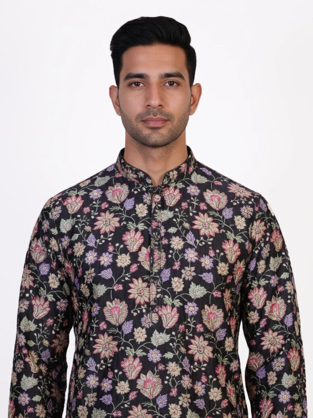 Man wearing a dark multi-color floral print kurta and white churidar pants, traditional ethnic wear.