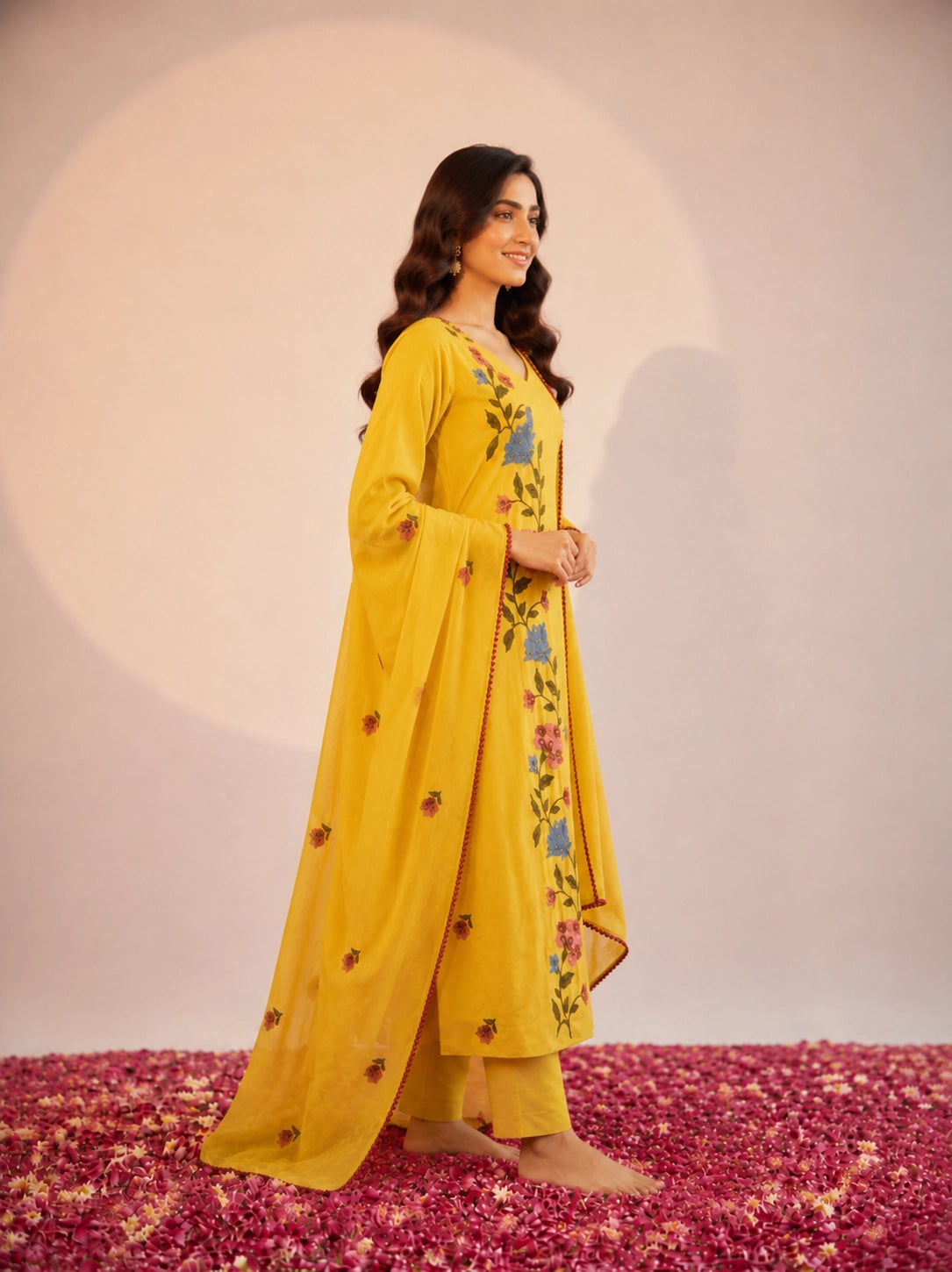 Woman in a vibrant yellow kurti set with colorful floral embroidery and dupatta.