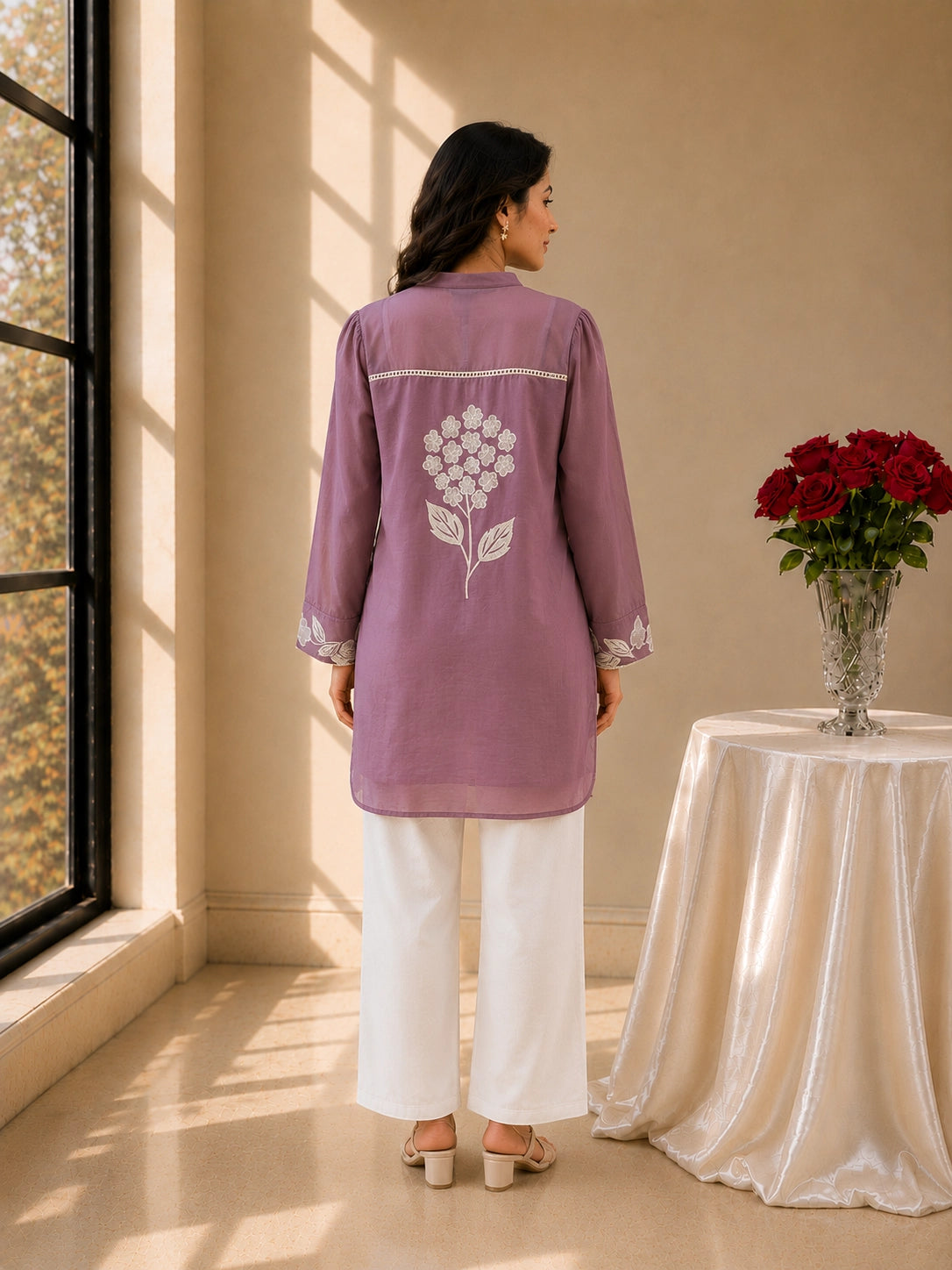 Smiling woman in a purple tunic with white floral embroidery and white pants.