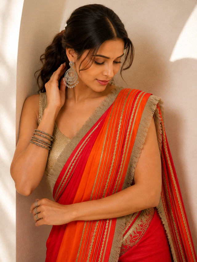 Woman elegantly draped in a vibrant red and orange ombre saree with silver borders.