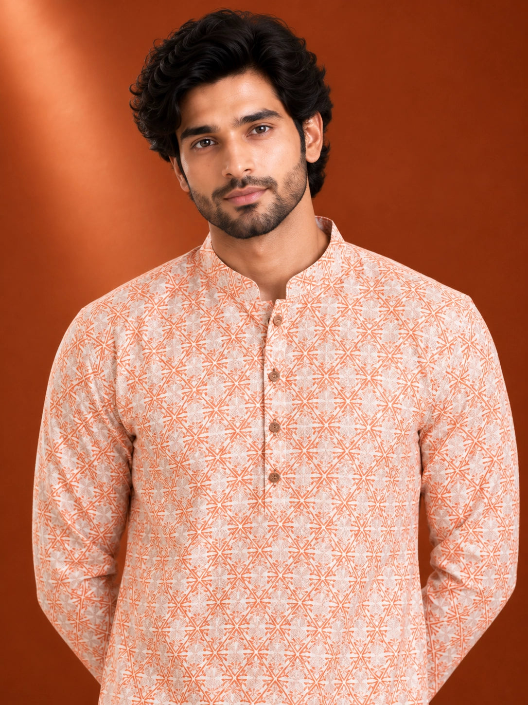 Man wearing an orange and white geometric printed kurta with white pajama and brown loafers.