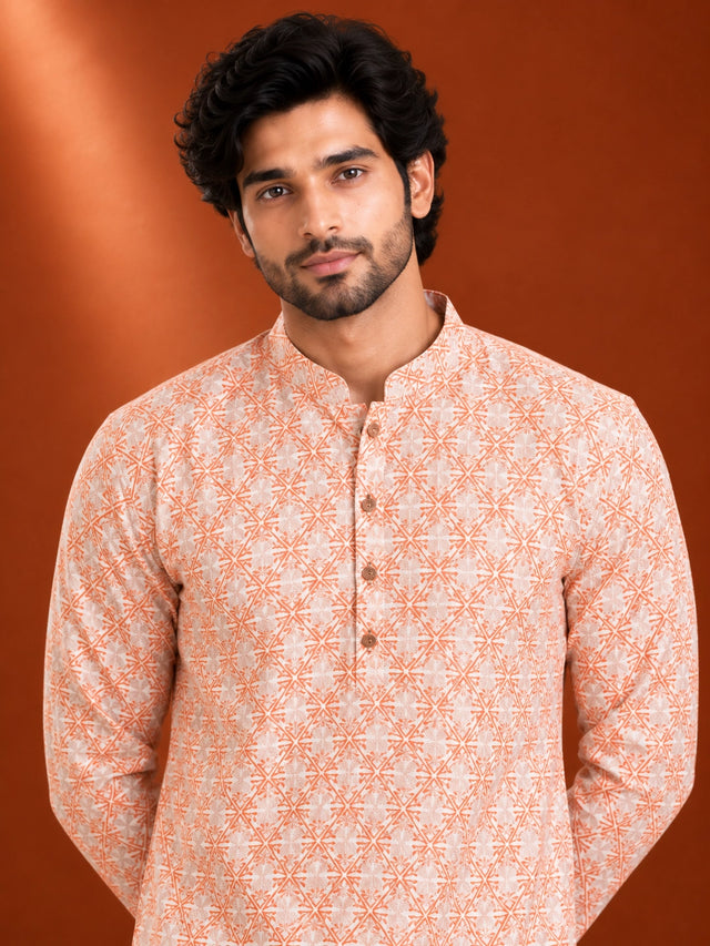 Man wearing an orange and white geometric printed kurta with white pajama and brown loafers.