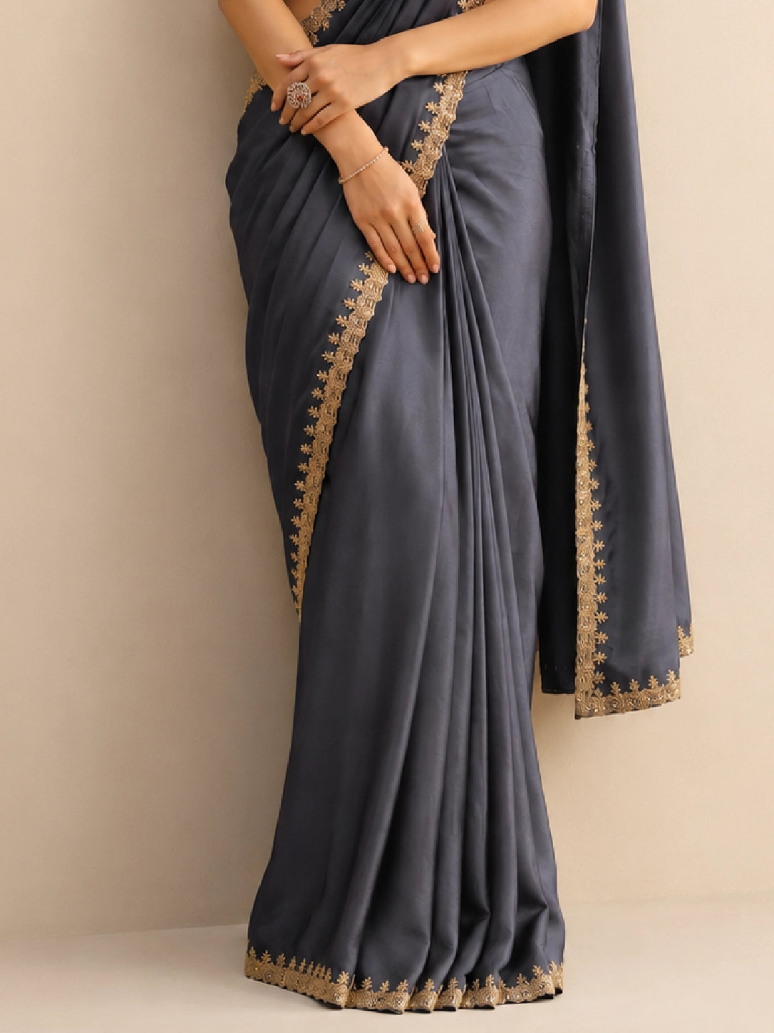 Woman wearing a flowing grey saree with an intricate golden border and a textured golden blouse.