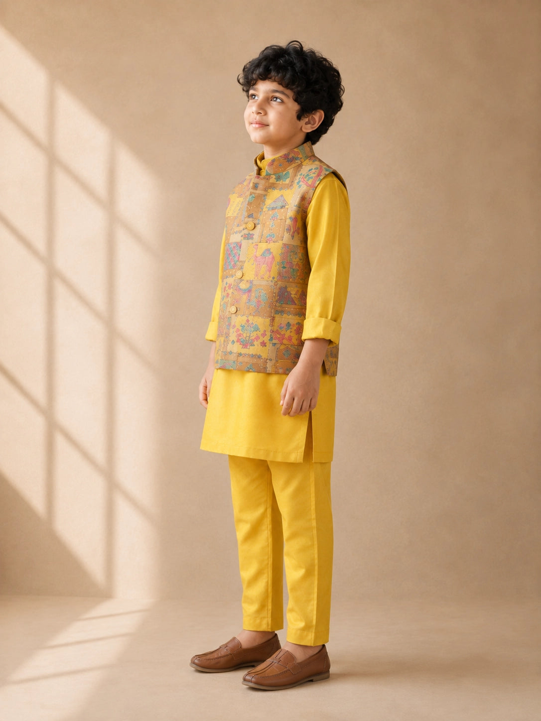 Young boy wearing a vibrant yellow kurta pajama and a colorful patterned Nehru jacket.