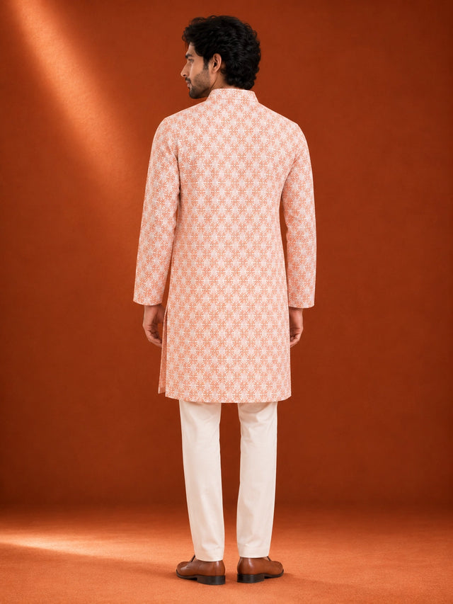 Man wearing an orange and white geometric printed kurta with white pajama and brown loafers.