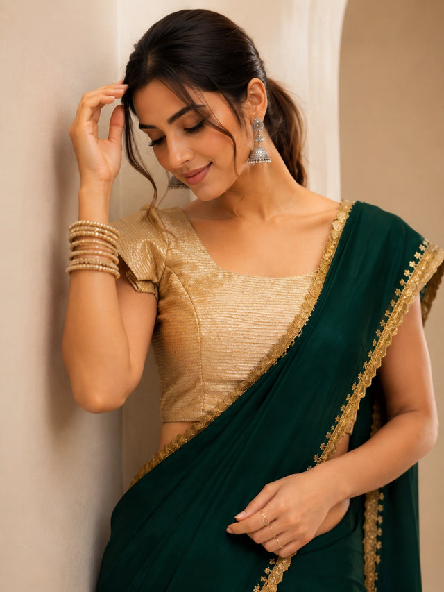 Woman wearing a beautiful emerald green saree with a golden border and matching blouse.