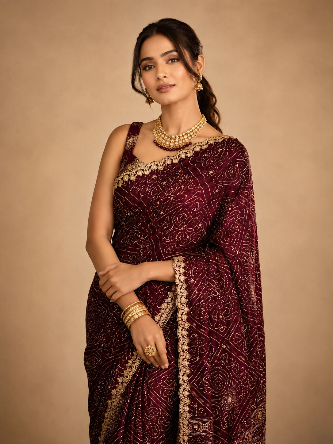 Woman in a maroon bandhani saree with intricate gold embroidery and border.