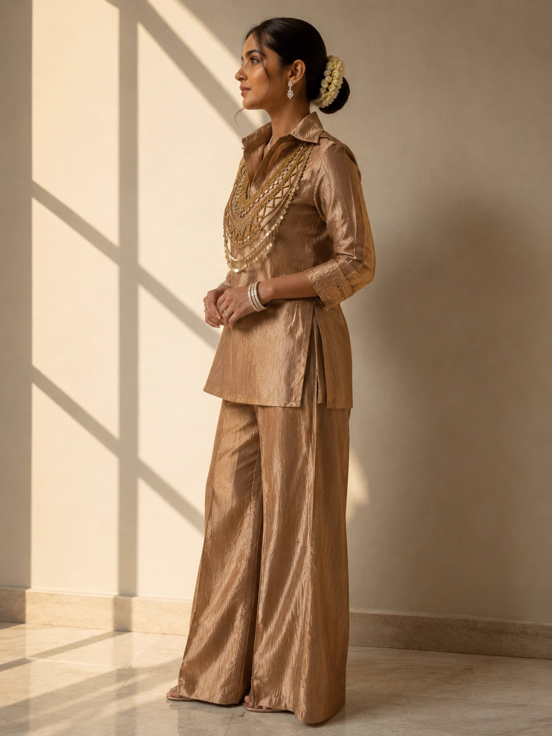 Woman wearing a shimmering brown kurti set with a heavily embroidered gold neckline.