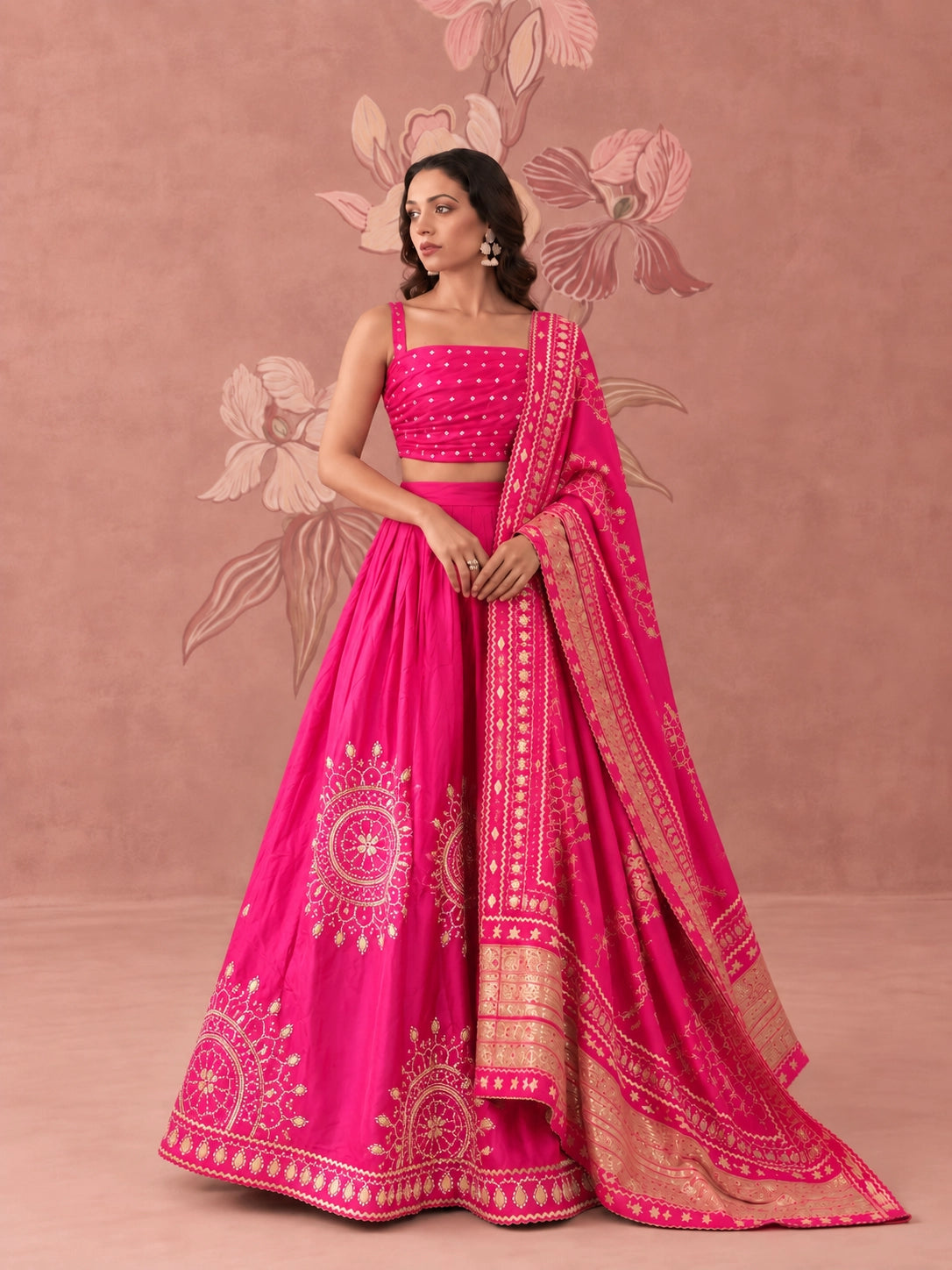 Woman wearing a vibrant rani pink lehenga set with intricate gold embroidery and matching dupatta.