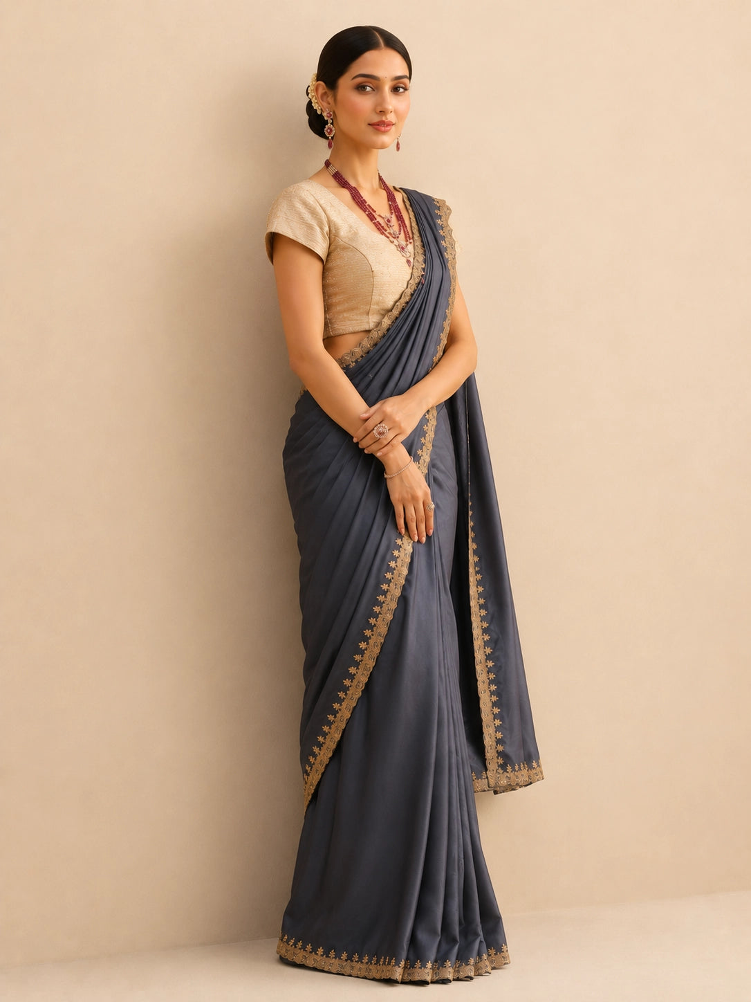 Woman wearing a flowing grey saree with an intricate golden border and a textured golden blouse.