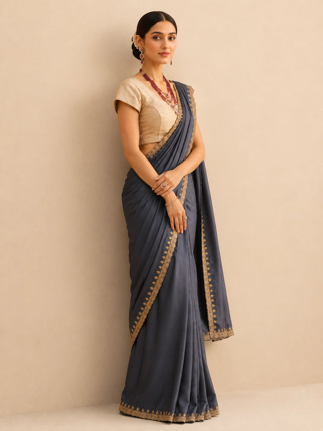 Woman wearing a flowing grey saree with an intricate golden border and a textured golden blouse.
