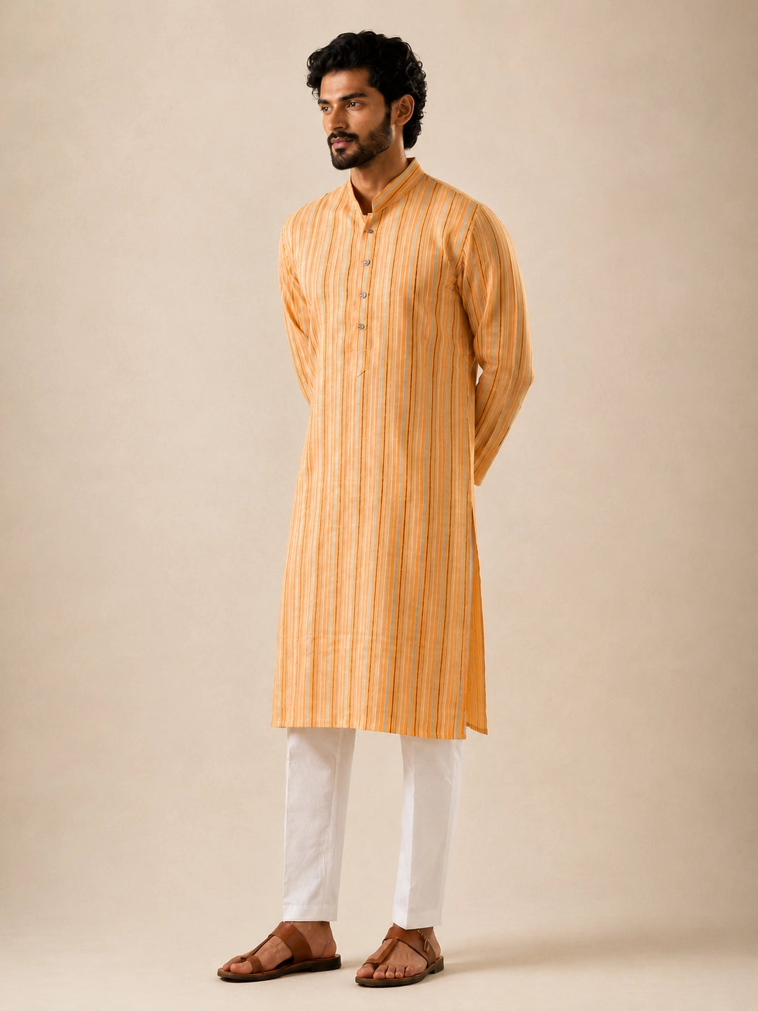 Man in a yellow striped kurta and white pajama, standing with hands behind back.