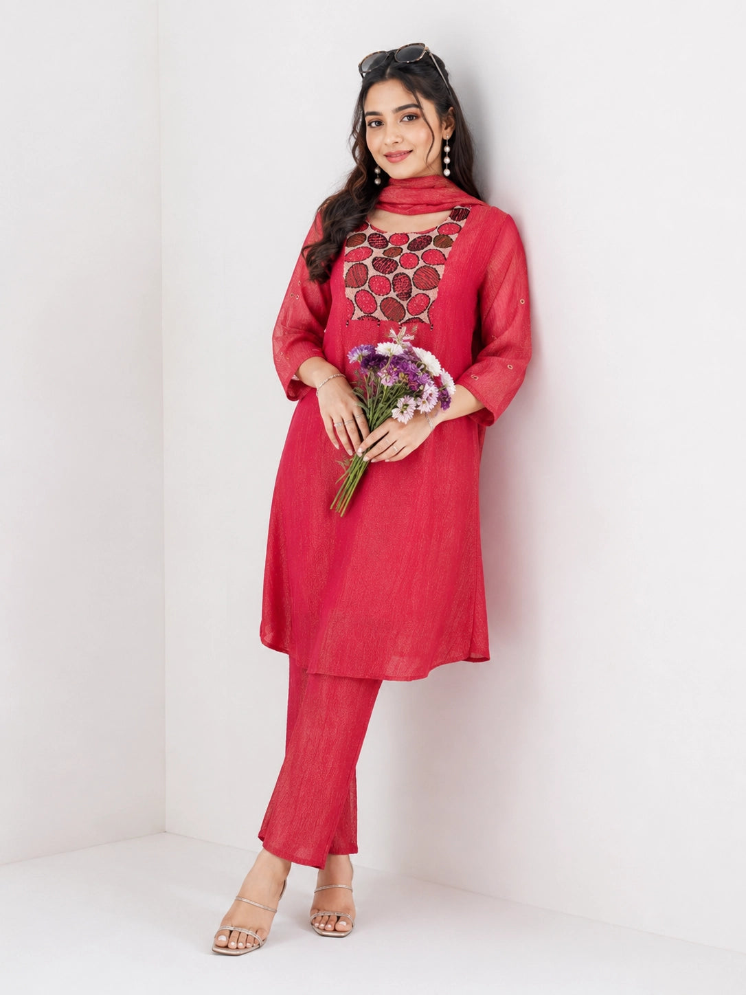 Woman wearing a Rani red Sharara with a geometric print yoke and matching dupatta, styled with pearl earrings.
