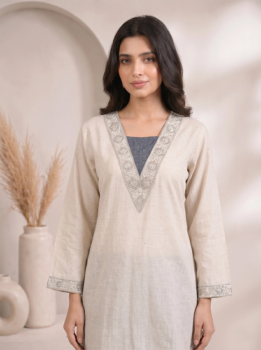 Woman wearing a beige embroidered V-neck kurta with dark blue palazzo pants, styled for a casual occasion.