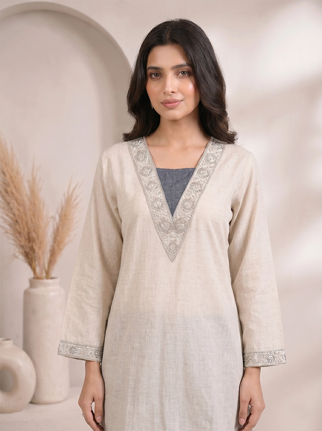 Woman wearing a beige embroidered V-neck kurta with dark blue palazzo pants, styled for a casual occasion.