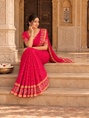 Woman in a vibrant red  saree with golden embroidery sitting on steps.