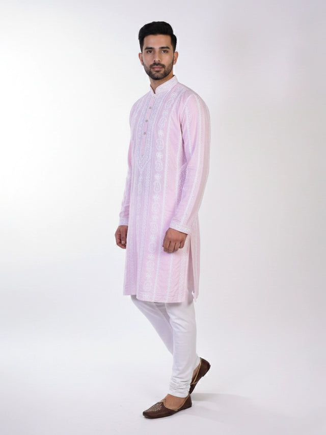 Man wearing a pink chikankari kurta with white churidar pants and brown embellished juttis.