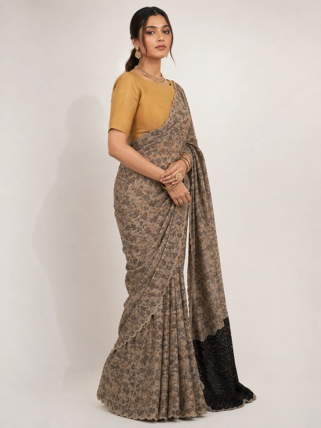 Woman wearing an elegant cream  printed saree with a gold blouse and embellished black pallu.