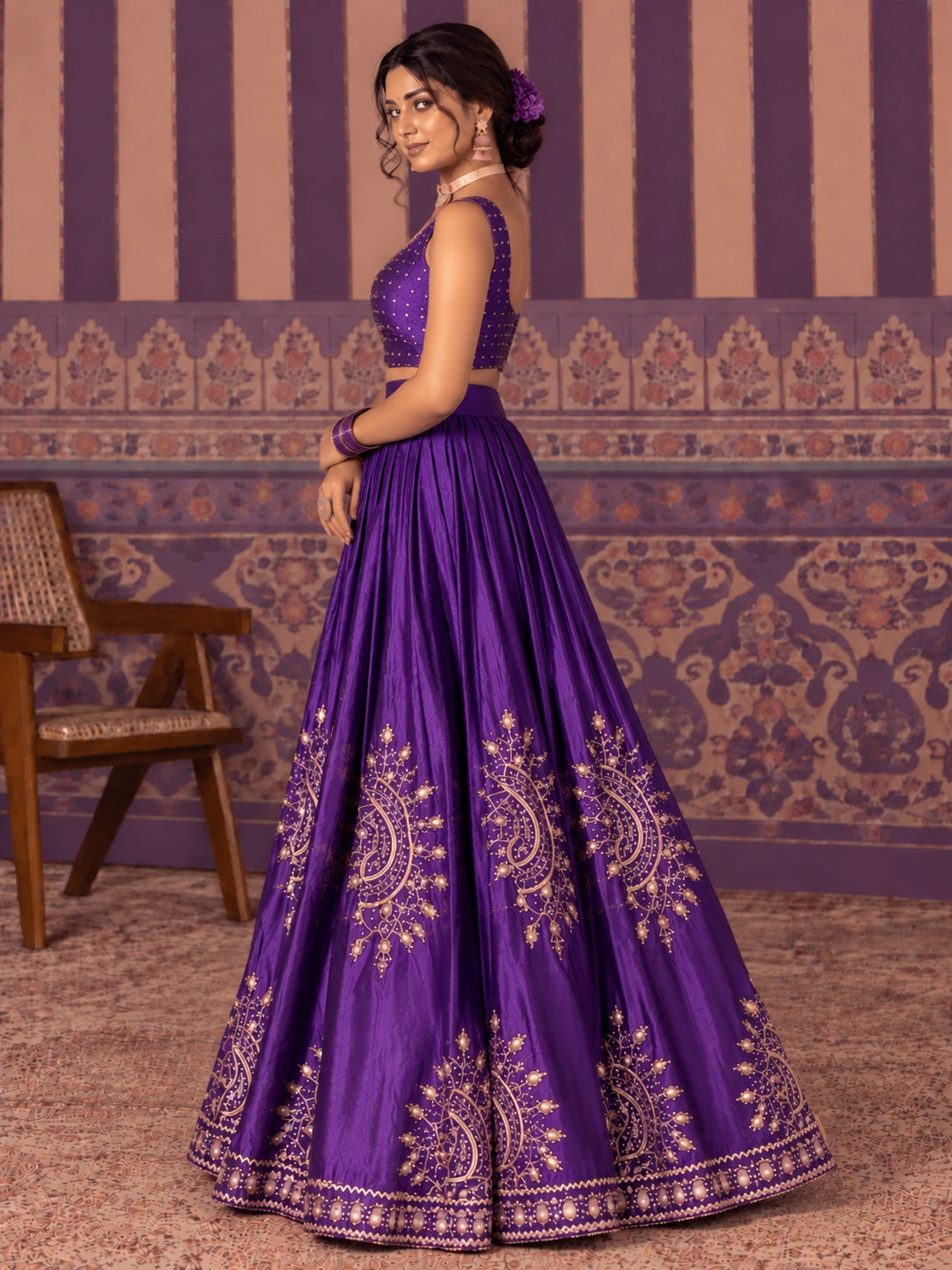 Woman in a vibrant purple embroidered lehenga choli set with gold patterns.