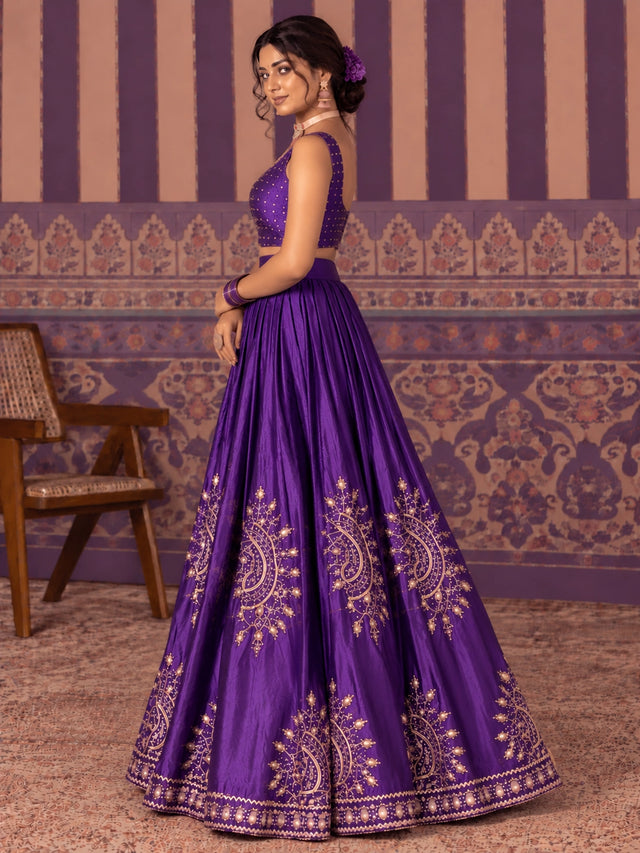 Woman in a vibrant purple embroidered lehenga choli set with gold patterns.