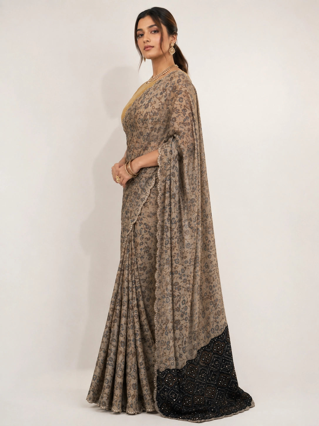Woman wearing an elegant cream  printed saree with a gold blouse and embellished black pallu.