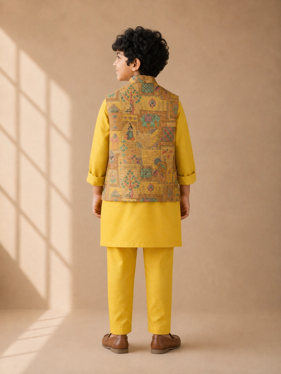 Young boy wearing a vibrant yellow kurta pajama and a colorful patterned Nehru jacket.