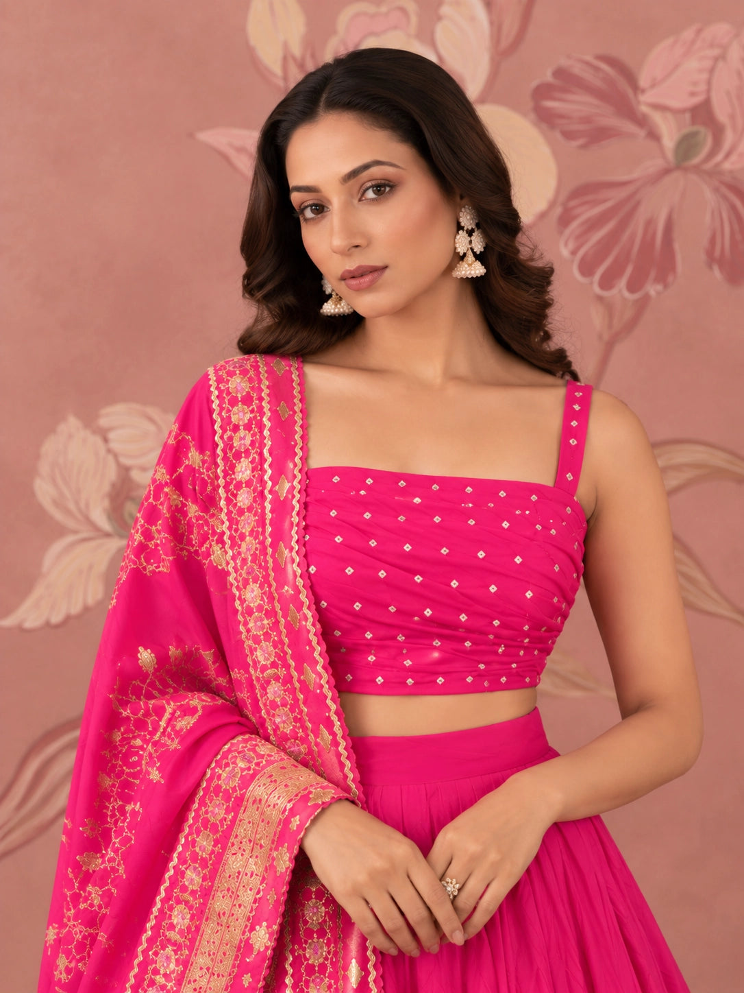 Woman wearing a vibrant rani pink lehenga set with intricate gold embroidery and matching dupatta.