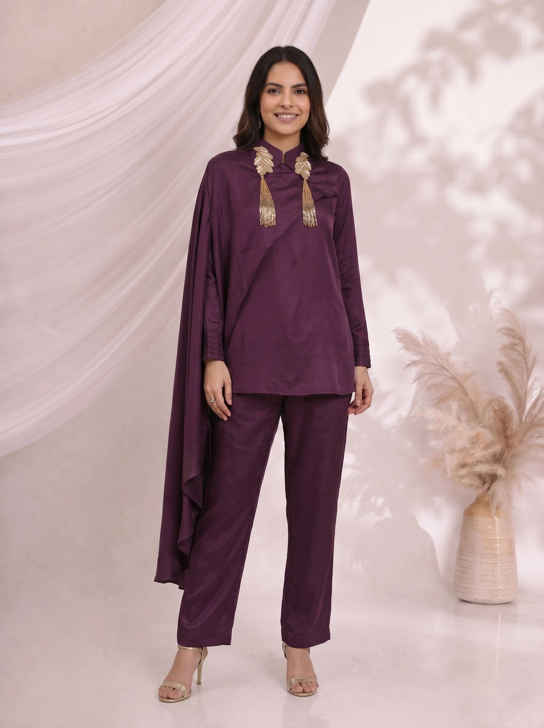 Woman wearing an elegant plum satin cape top and matching pants, styled for an evening event.