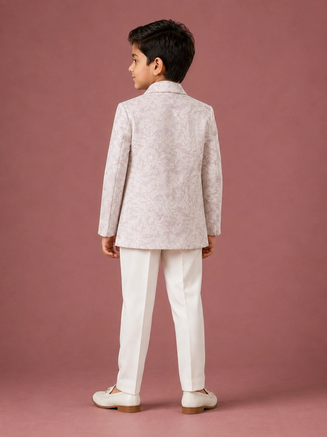 Young boy in a light pink patterned IndoWestern jacket, white kurta, and white trousers.