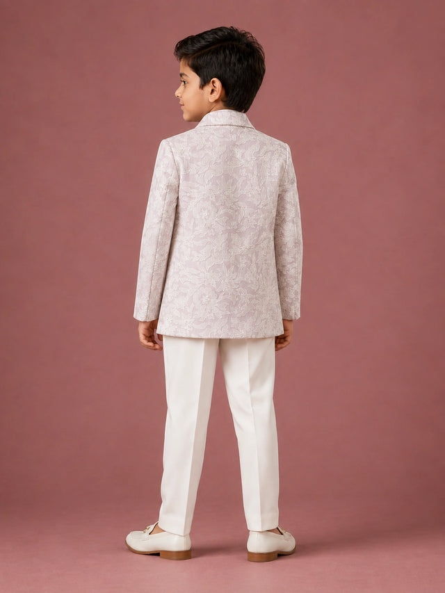 Young boy in a light pink patterned IndoWestern jacket, white kurta, and white trousers.