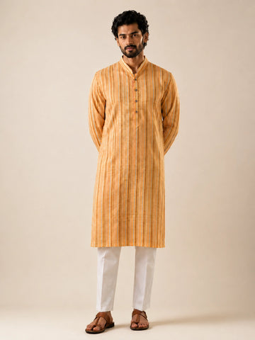 Man in a yellow striped kurta and white pajama, standing with hands behind back.