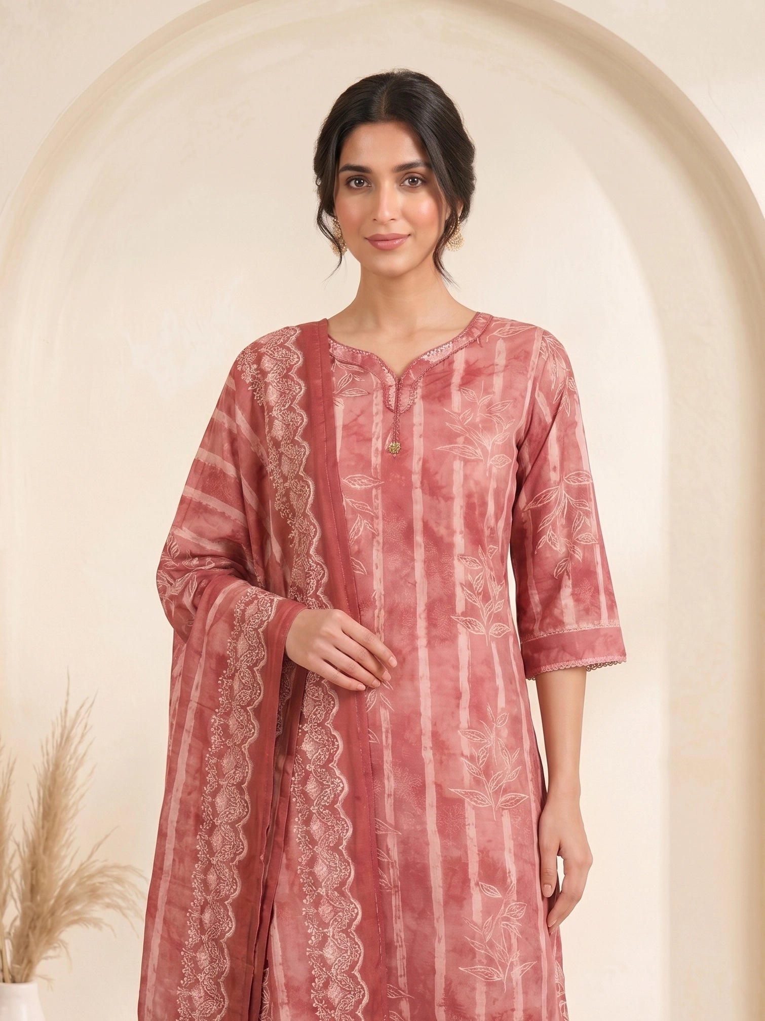 Woman wearing a rose pink printed kurti set with a dupatta, featuring leaf motifs and striped patterns.