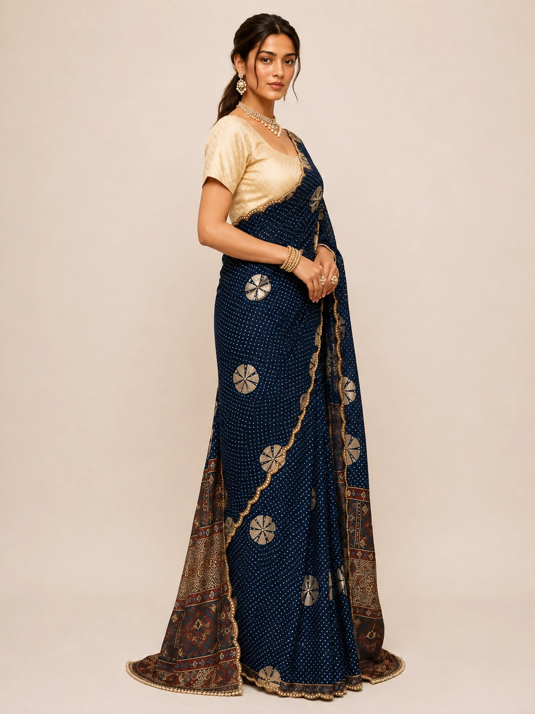 Woman in navy blue bandhani saree with cream blouse and gold jewelry.