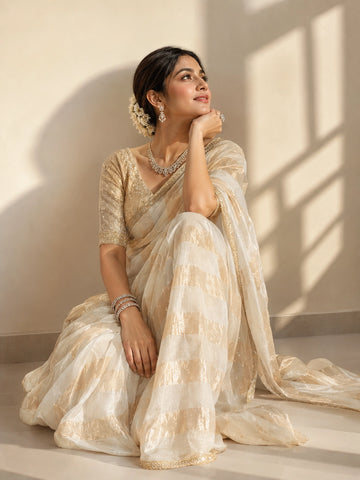 Woman in a cream and gold striped saree with an embroidered blouse.
