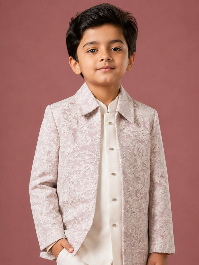 Young boy in a light pink patterned IndoWestern jacket, white kurta, and white trousers.