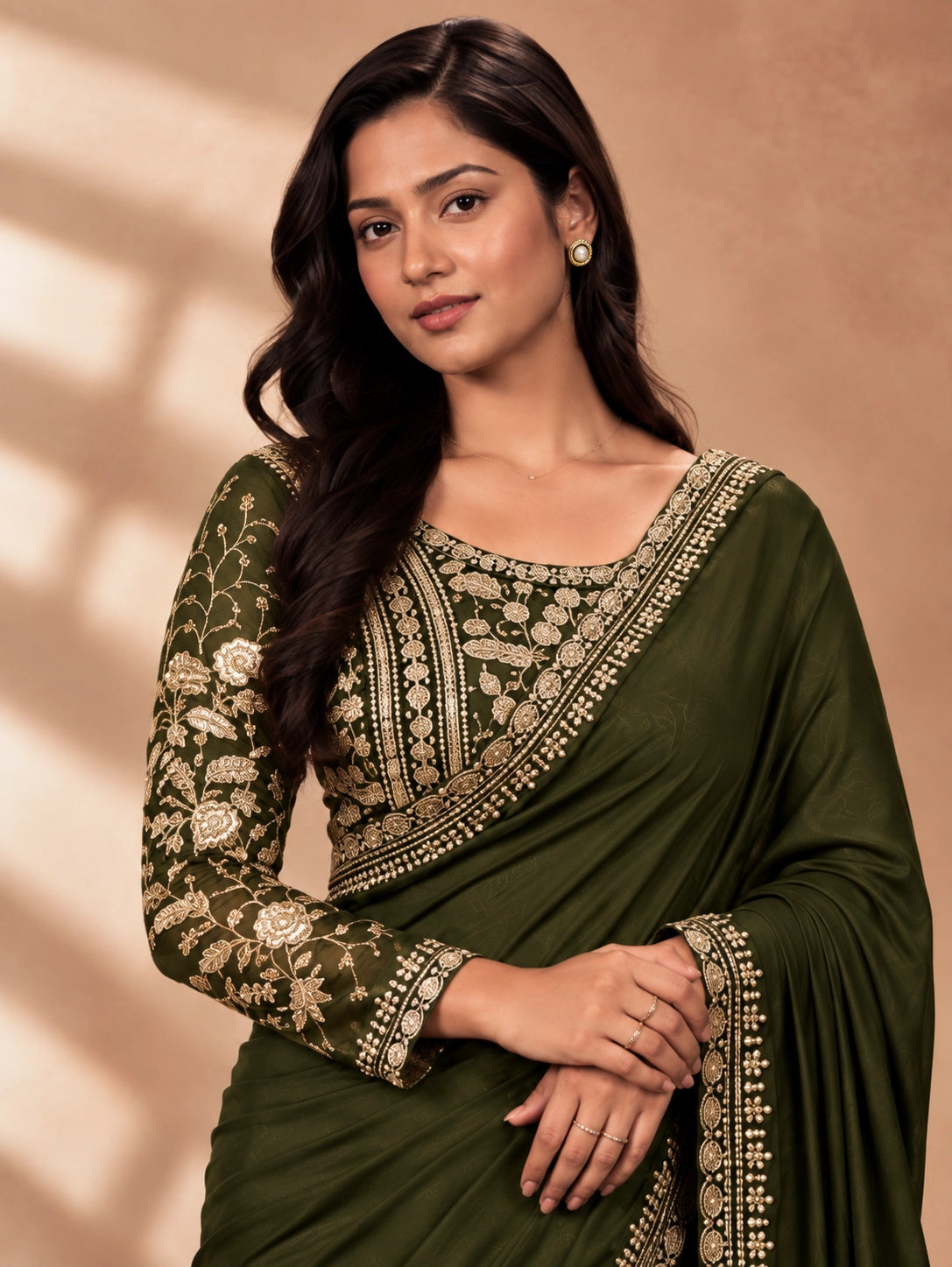 Woman in a flowing mehndi green saree with intricate gold embroidery on blouse and border.
