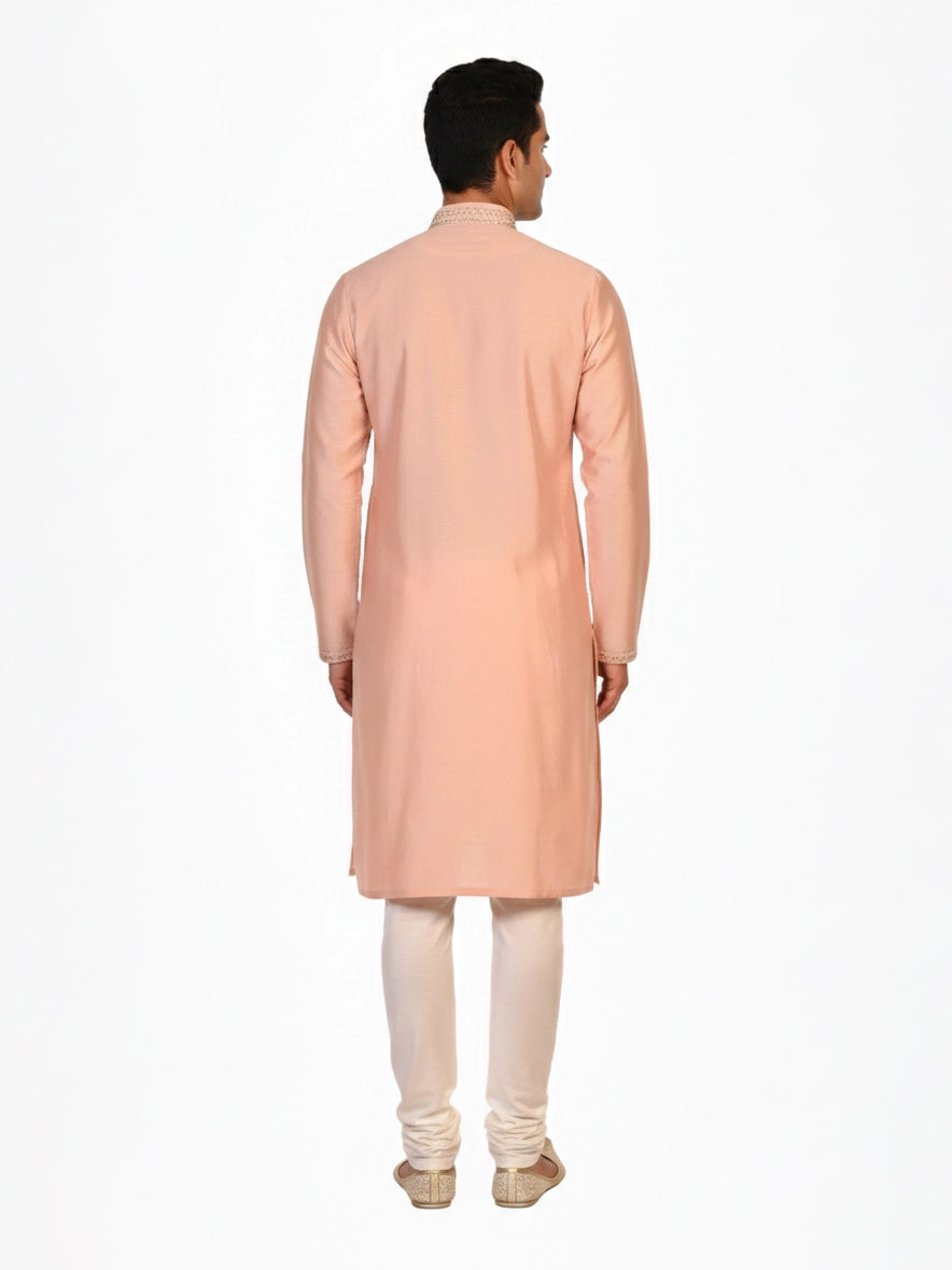 Man wearing a peach silk Kurta Pajama with intricate embroidery on the neckline and cream churidar pants.