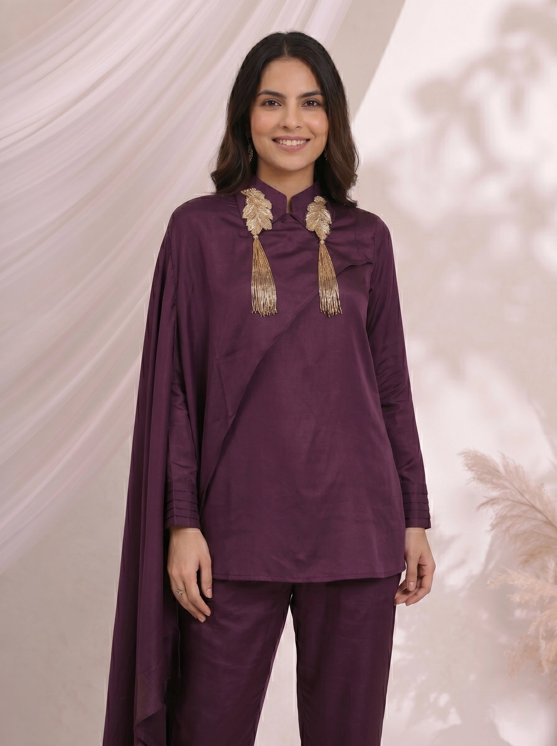 Woman wearing an elegant plum satin cape top and matching pants, styled for an evening event.