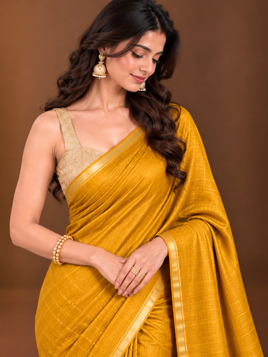 Woman modeling an elegant mustard yellow saree with a subtle woven pattern and golden border.
