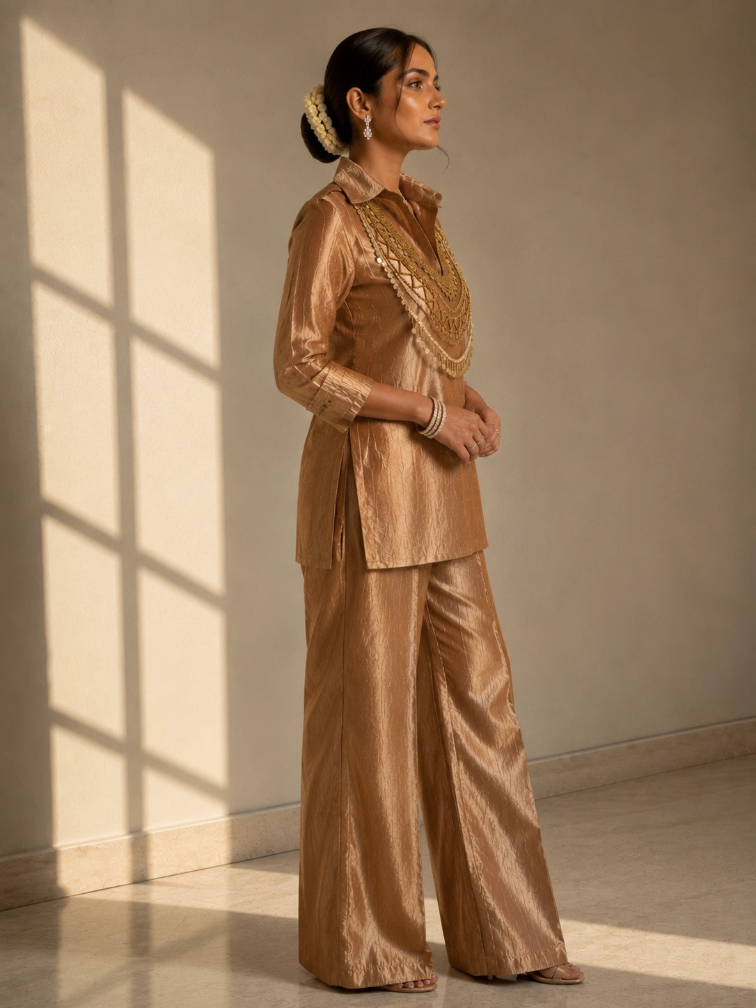 Woman wearing a shimmering brown kurti set with a heavily embroidered gold neckline.