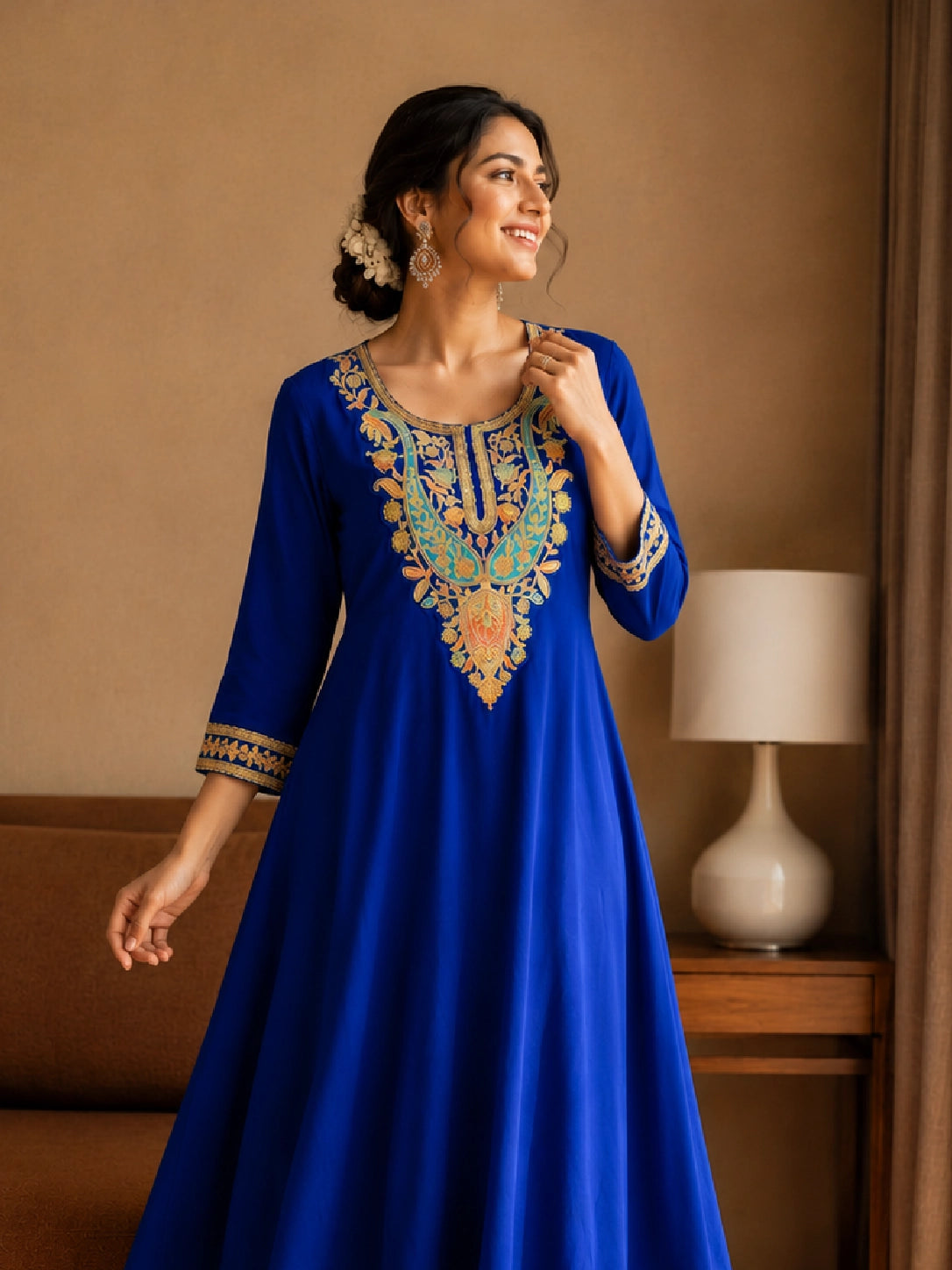 Woman in royal blue embroidered kurta with red pants, sitting by window.