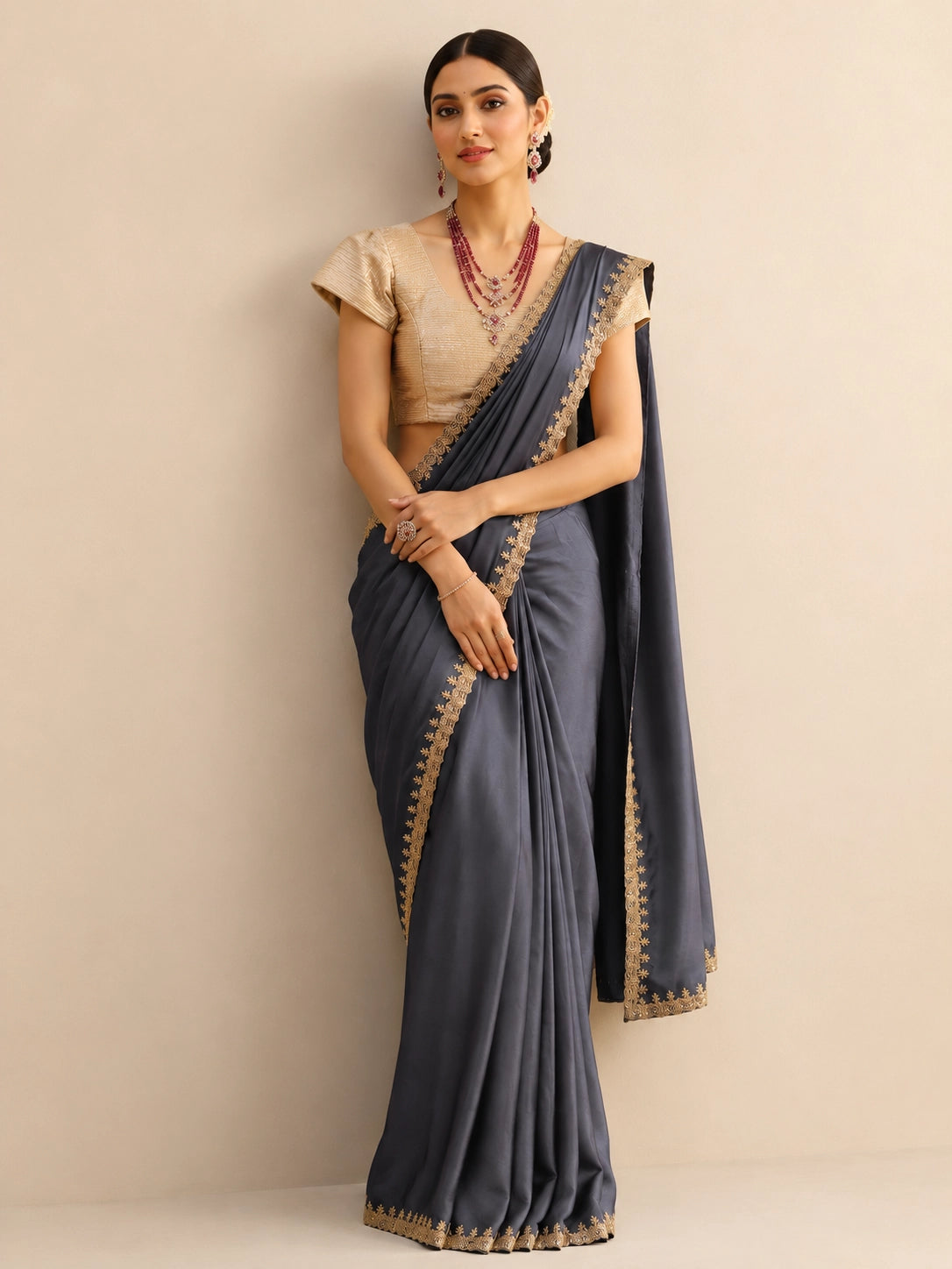 Woman wearing a flowing grey saree with an intricate golden border and a textured golden blouse.
