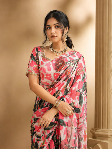 Woman wearing a vibrant pink floral saree with a matching blouse and traditional jewelry.