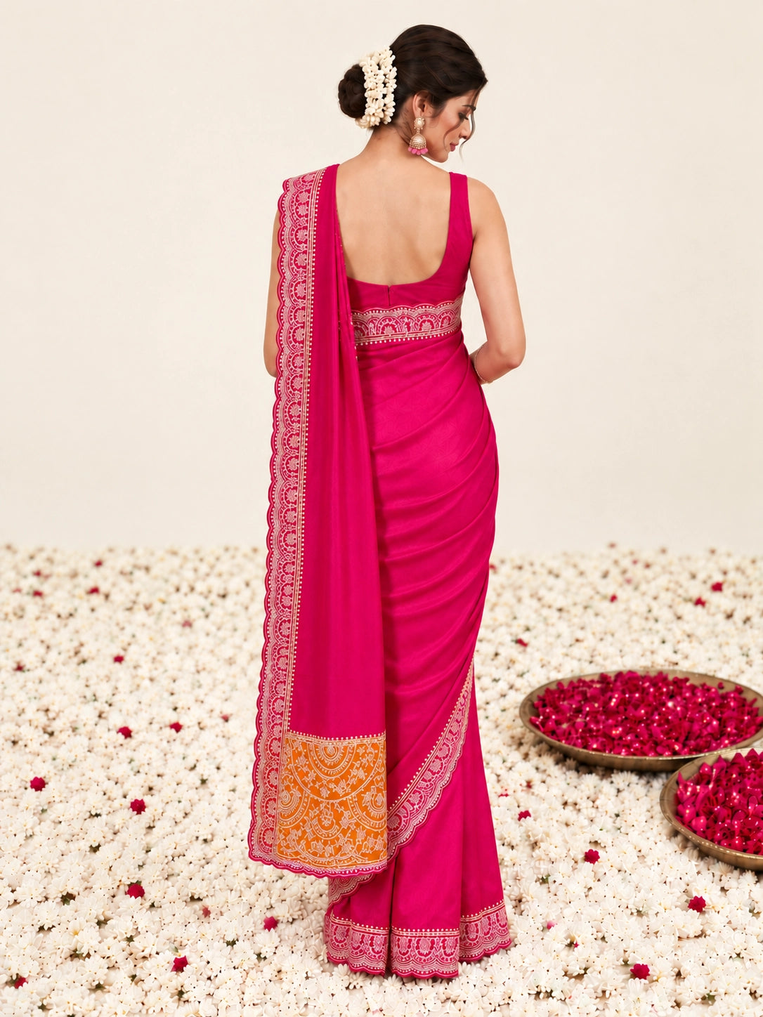 Woman in a vibrant RANI  saree with gold border, sitting among white flowers.