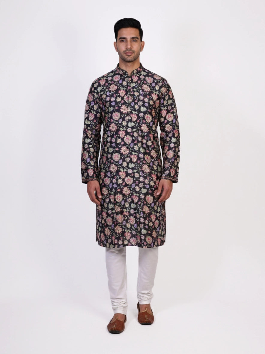 Man wearing a dark multi-color floral print kurta and white churidar pants, traditional ethnic wear.