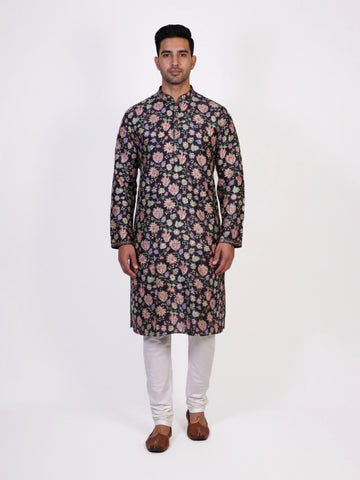 Man wearing a dark multi-color floral print kurta and white churidar pants, traditional ethnic wear.