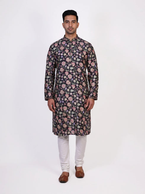 Man wearing a dark multi-color floral print kurta and white churidar pants, traditional ethnic wear.