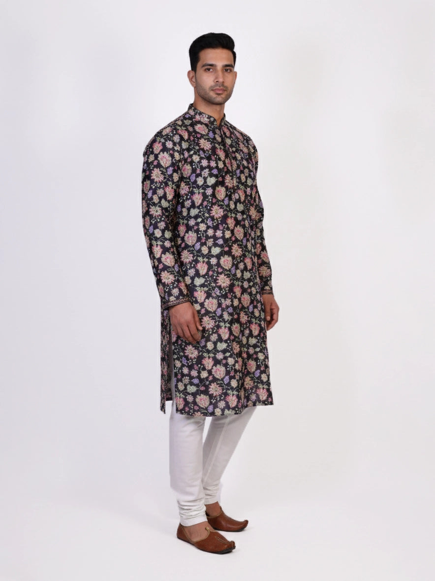 Man wearing a dark multi-color floral print kurta and white churidar pants, traditional ethnic wear.