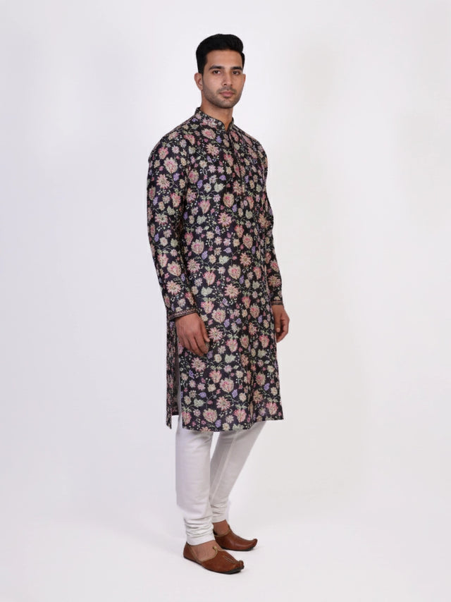 Man wearing a dark multi-color floral print kurta and white churidar pants, traditional ethnic wear.