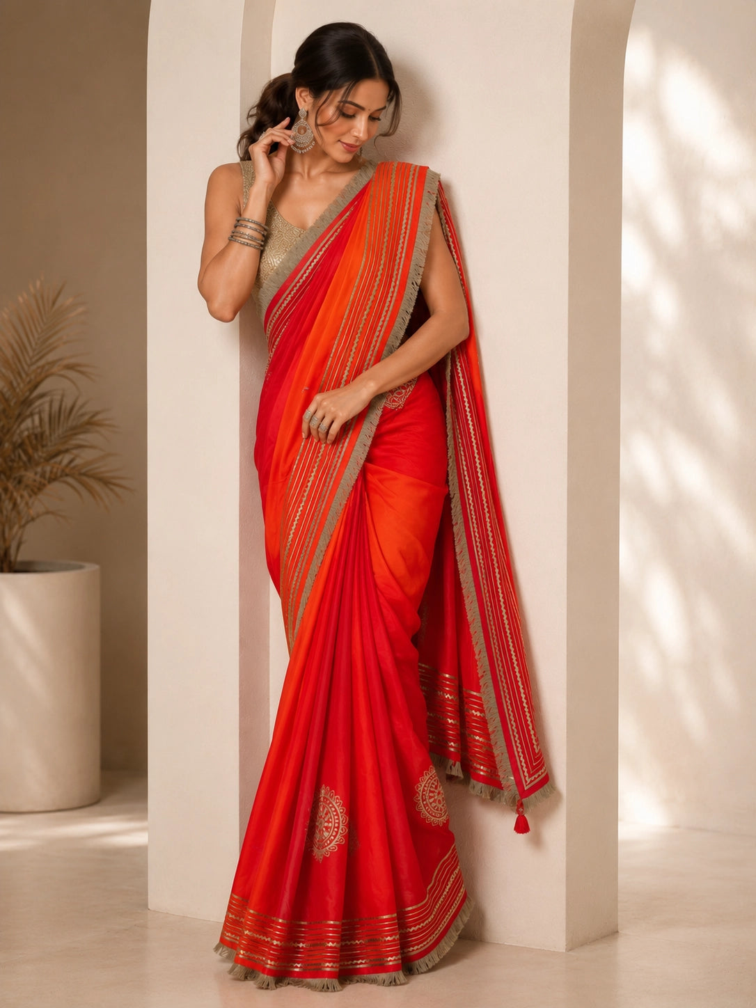 Woman elegantly draped in a vibrant red and orange ombre saree with silver borders.